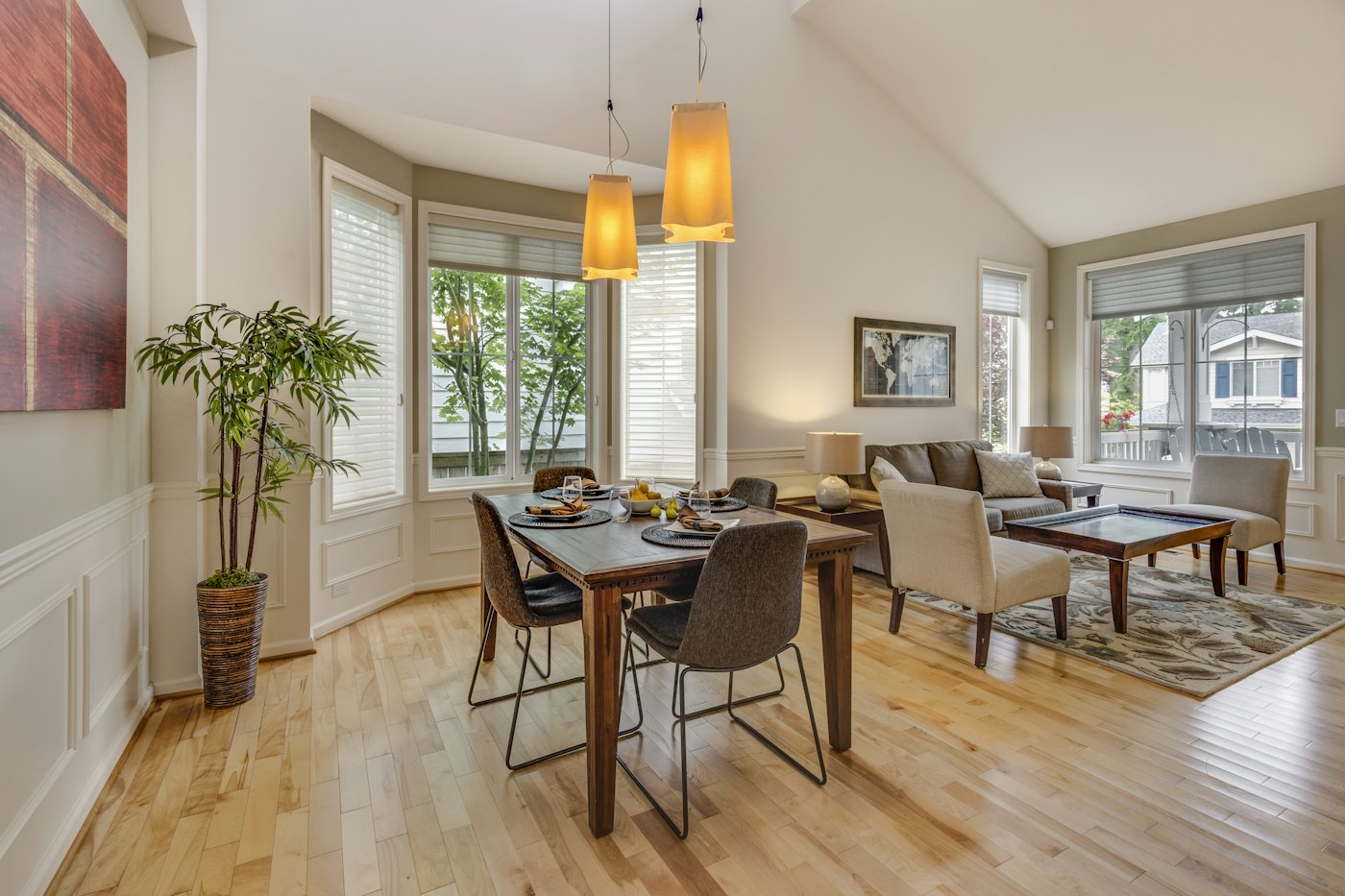Dining and living space with a wooden table beside bay windows