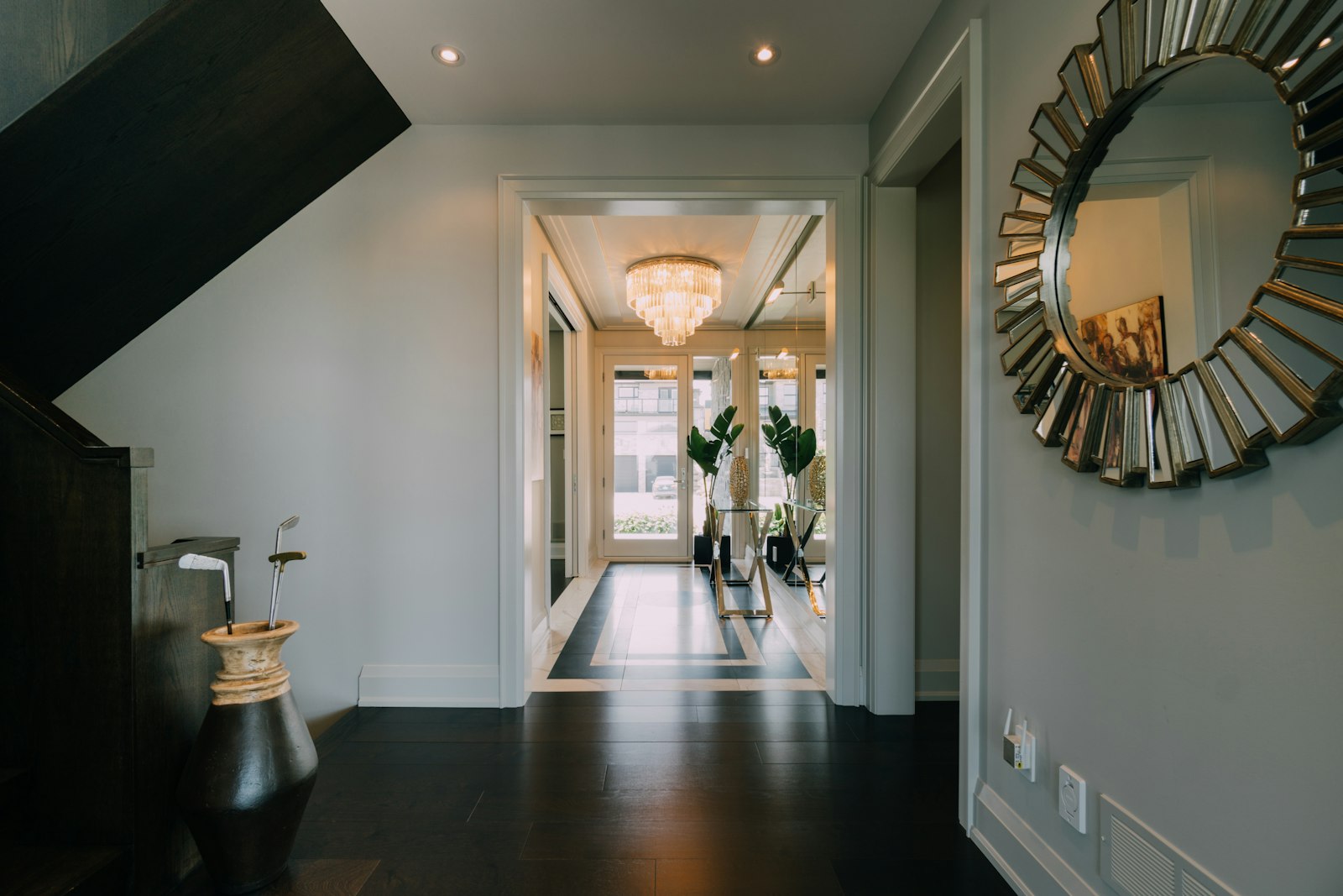 Bright foyer with a chandelier, sunburst mirror and dark wood floor
