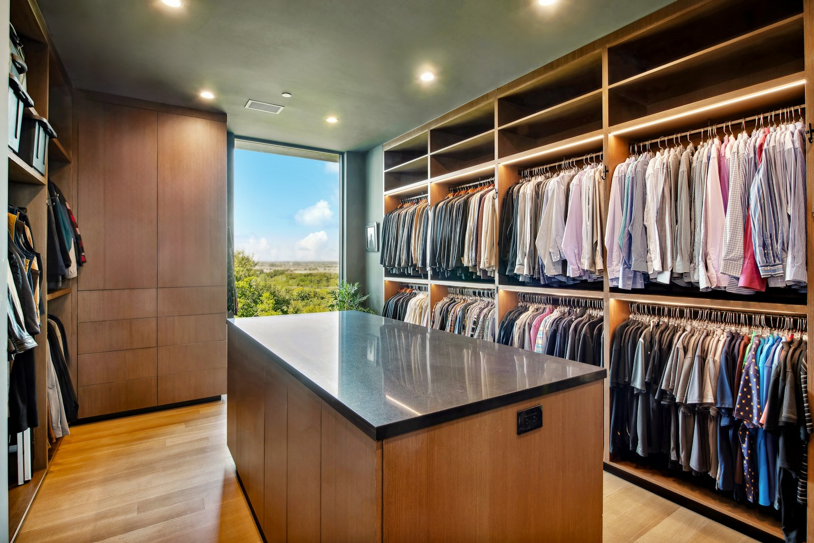 Walk-in closet with lit wooden hanging rails, tall storage and a stone-top island